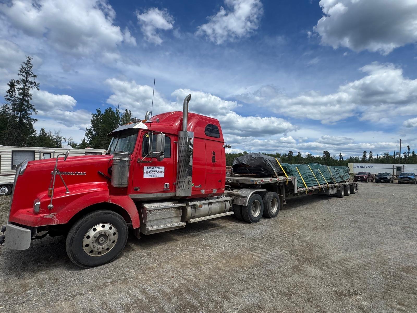 Red semi truck with a loaded step deck trailer for heavy hauling from Thunder Bay