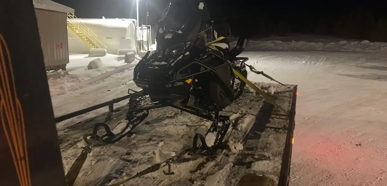 Snowmobile strapped down on a trailer at night