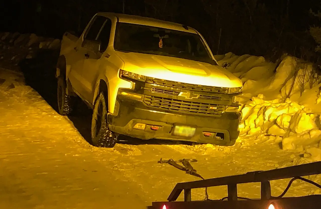 Pickup truck stuck in a snowbank at night, lit by tow truck lights, before a winch-out